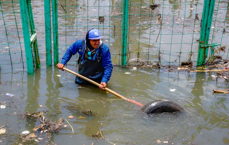 Man removing debris from flooded polluted water with a stick, highlighting urban pollution.